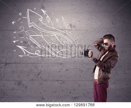 A hipster guy opening his point of view through looking a vintage camera concept with illustratied drawn arrows on urban wall