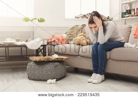 Desperate Helpless Woman Sitting On Sofa In Messy Living Room. Young Girl Surrounded By Many Stack O