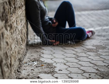 substance abuse, addiction, people and drug use concept - close up of addict woman and used syringes on ground