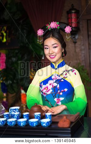 Asian traditions and culture. Young beautiful chinese woman in traditional dress getting ready to perform tea ceremony with tea tools on the table