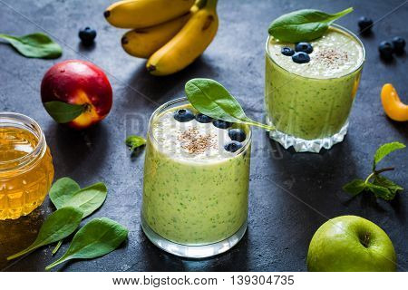 Detox green smoothies. Still life of green smoothie with fruits, honey and spinach leaves. Ultra healthy detox green smoothie with spinach, chia seeds, bananas, green apple, plain yogurt and honey on slate background