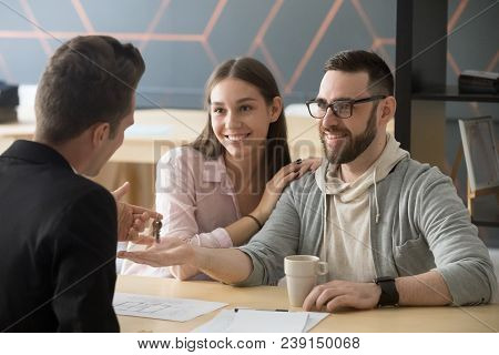 Happy Millennial Couple Getting Keys To New Home From Realtor, Customers Renters Tenants Make Deal B