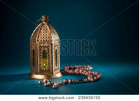 A golden Ramadhan lamp with Islamic rosary beads on dark background. Ramadan - an important Islamic festival. Islamic festive greeting card photo.