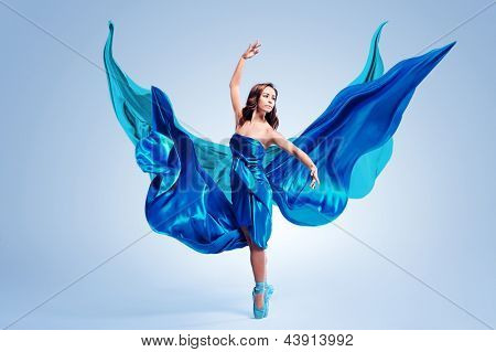 Beautiful ballet dancer with flowing blue fabric dancing with grace in studio