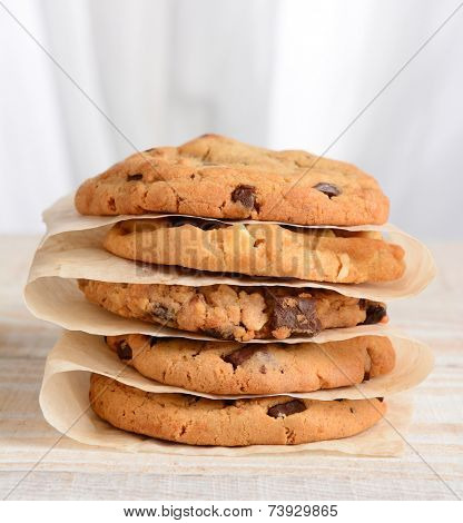 Closeup of a stack of fresh baked cookies Chocolate Chip, Oatmeal Raisin, White Chocolate Chip cookies on parchment paper. Square format on a rustic white kitchen table.