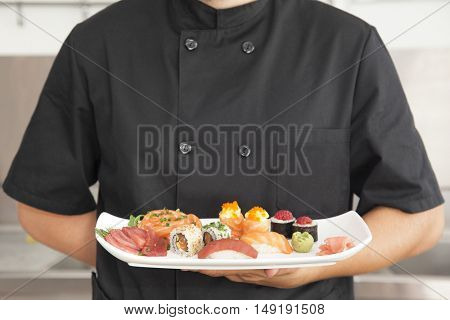 Male chef holding a plate full of sushi at the kitchen