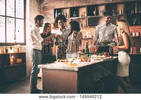 Enjoying party with nearest friends. Group of cheerful young people enjoying home party with snacks and drinks while communicating on the kitchen