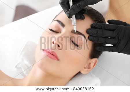 Young woman undergoing procedure of eyebrow permanent makeup in beauty salon