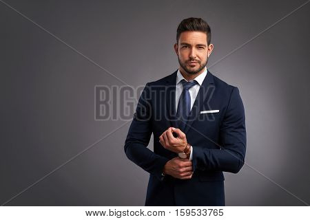 A confident elegant handsome young man standing in front of a grey background in a studio wearing a nice suit