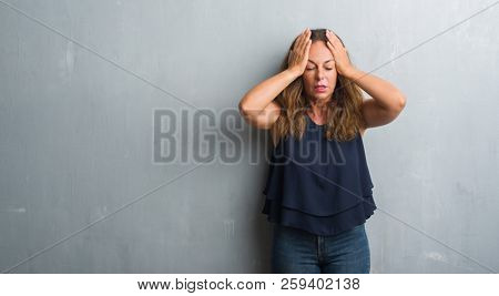 Middle age hispanic woman standing over grey grunge wall suffering from headache desperate and stressed because pain and migraine. Hands on head.