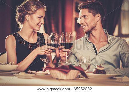 Beautiful young couple with glasses of red wine in luxury restaurant