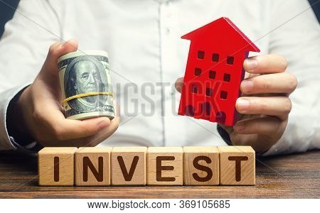 A Man With Dollars And A House Figurine And The Word Invest. Real Estate Financial Investment. Favor