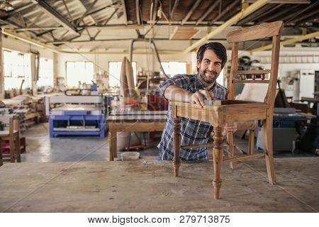 Smiling Furniture Maker Sanding A Chair In His Woodworking Shop