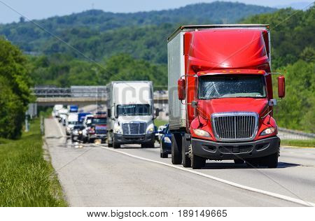 A red semi leads a line of traffic down an interstate highway in Tennessee. Heat rising from the pavement gives background trucks and forest a cool shimmering effect.