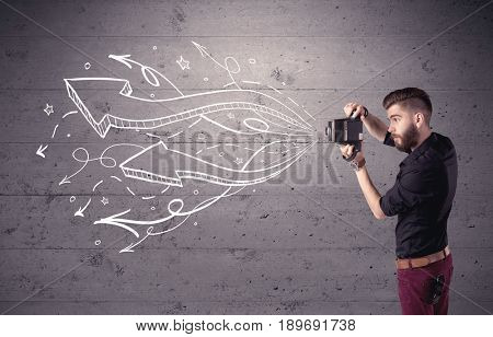 A hipster guy opening his point of view through looking a vintage camera concept with illustratied drawn arrows on urban wall