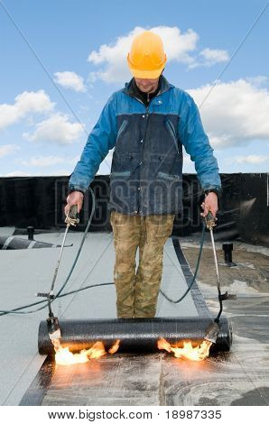 Roofing felt installation with heating and melting roll of bitumen roll by torch on flame