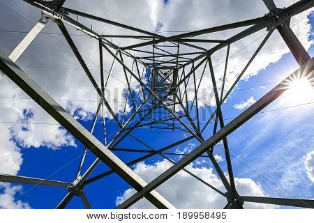 The electricity transmission pylon in daytime outdoors. Electricity tower standard overhead power line transmission tower on the background blue sky and white cloud.