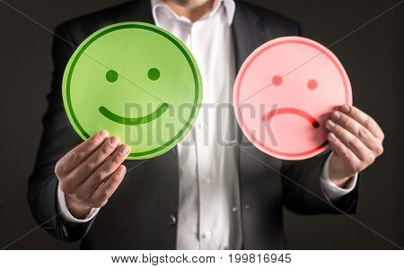 Business man with happy smiling and sad unhappy cardboard paper smiley face emoticon. Rating and giving review about customer satisfaction or team spirit in company.