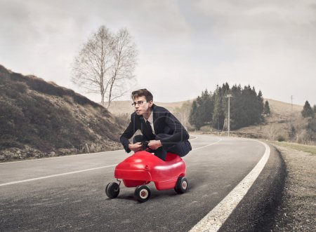 Foto de Joven hombre de negocios conduciendo un coche de juguete en una carretera rural - Imagen libre de derechos