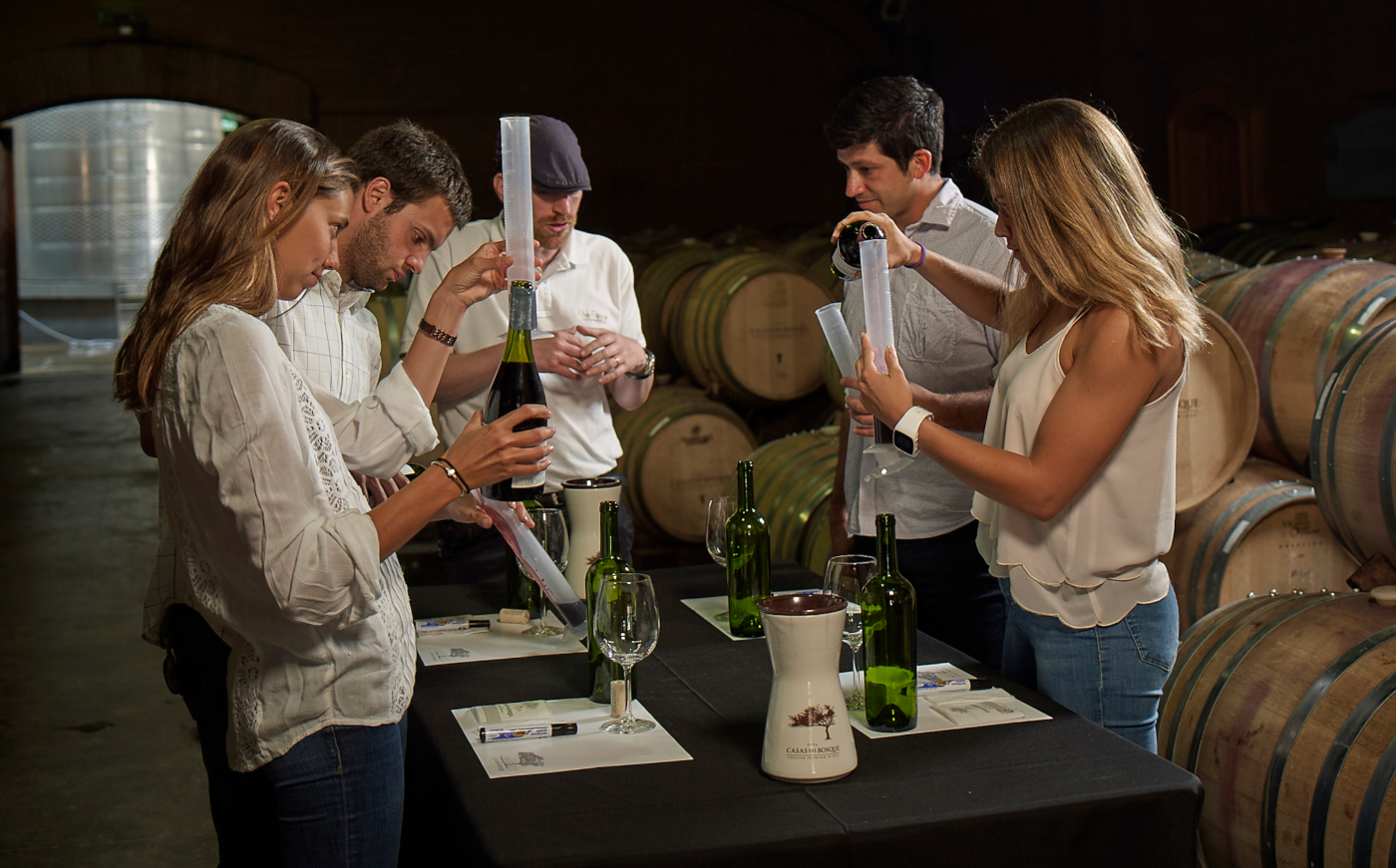 Imagen de un grupo de turistas realizando una cata de vino profesional en medio de un sala de barricas de la viña chilena Santa Carolina.