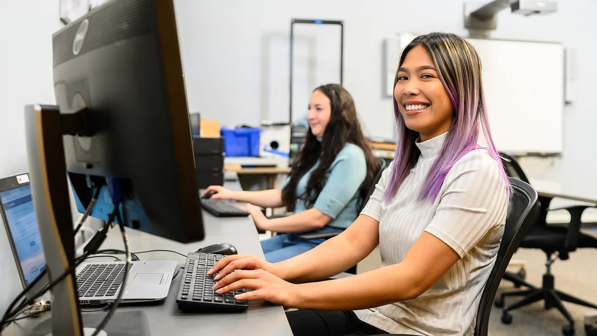 Two women working on their computers, one looking at the camera and smiling