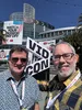 Rene and Todd posing at VidCon in front of a sign that reads "watch your passion pay off"