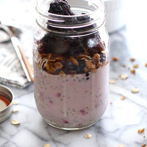 Side view of mason jar filled with berry chia overnight oats, and granola and fruit.