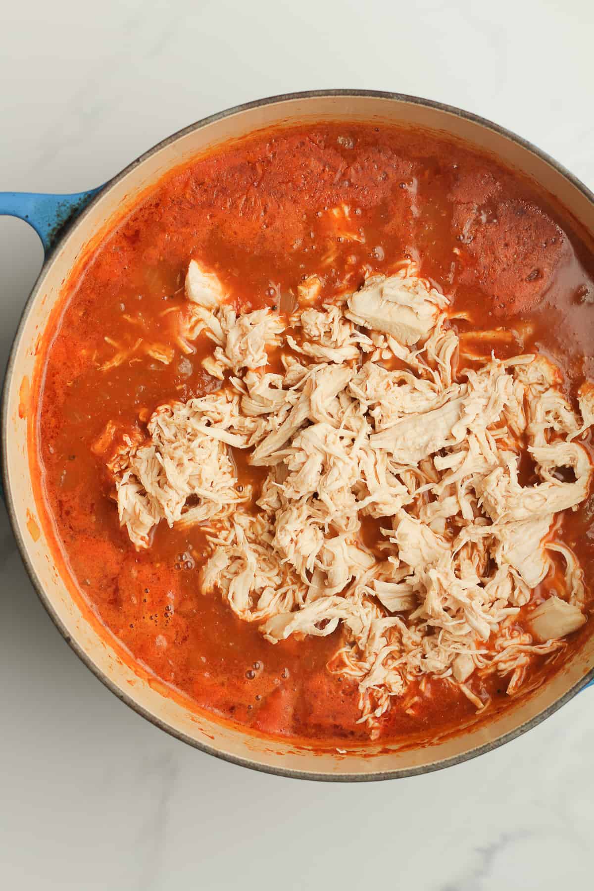 A stock pot of the soup with the shredded chicken on top.