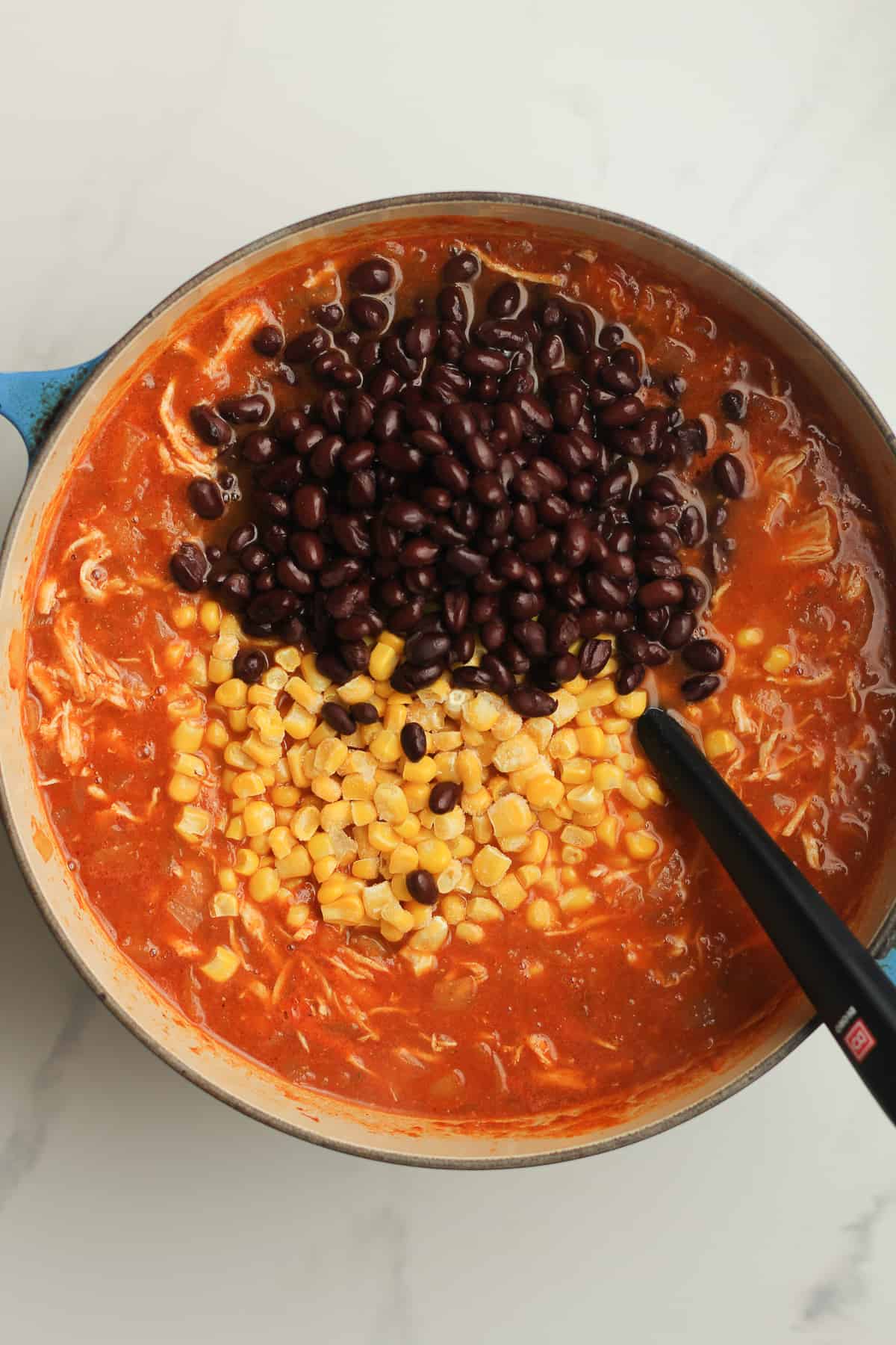 The stock pot of chicken tortilla soup with black beans and corn on top.