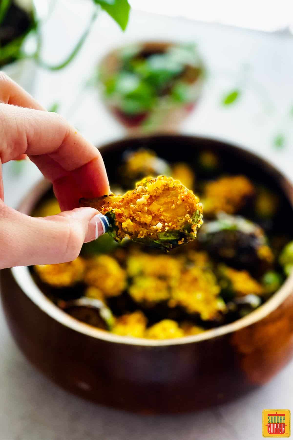 Holding an air fried brussels sprout over a bowl of sprouts