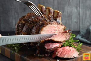 slicing into standing rib roast on a wood cutting board