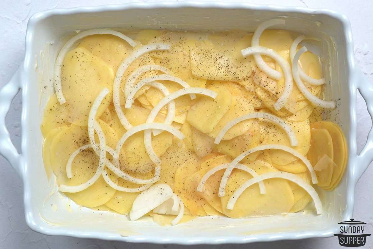 layering scalloped potatoes in a white casserole dish