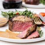 A medium rare cooked filet mignon shown drizzled with black peppercorn sauce.