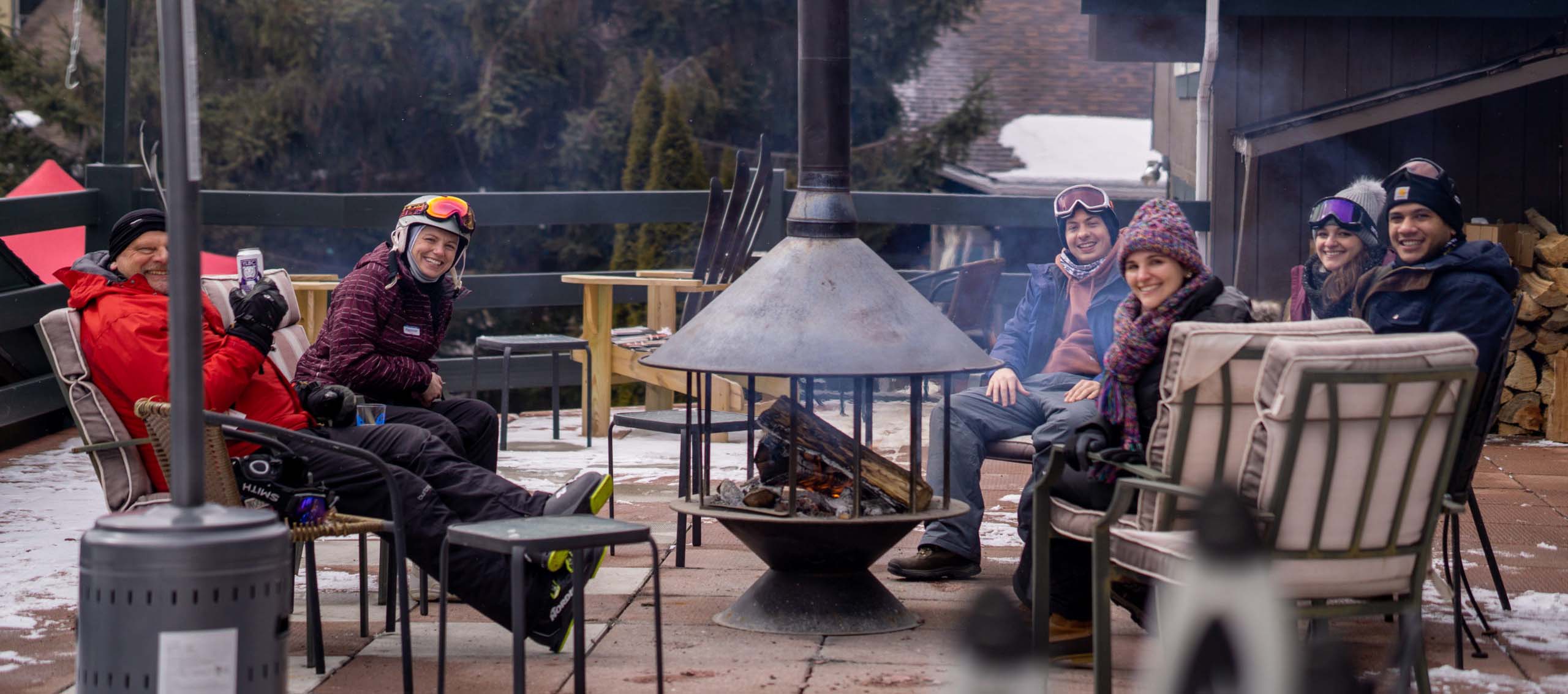 People gathered around a fire pit on an outdoor deck in winter at a ski lodge