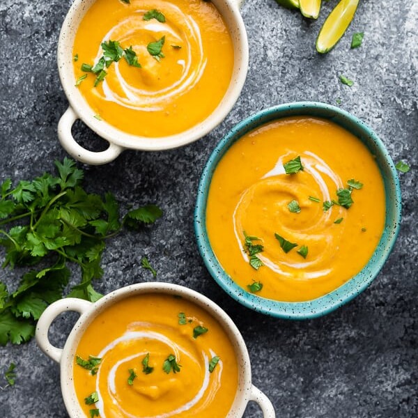 overhead shot of three blue and white bowls filled with thai curry sweet potato soup on gray background