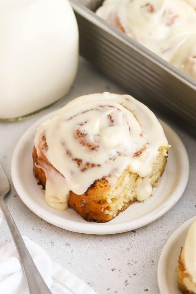 gluten-free cinnamon roll on a white plate next to a bottle of milk