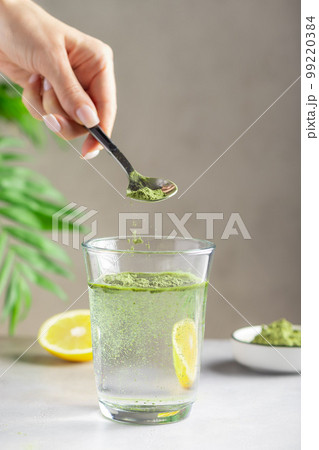 female hand pouring green superfood powder into glass of water. 99220384