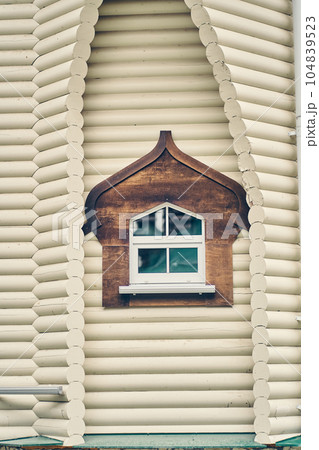 Decorative window with a dark frame in a white wooden house. The facade of the building. Russian traditional national folk style in wooden architecture. High quality photo 104839523