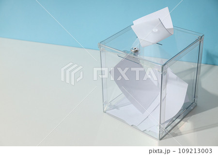 Voting box with papers on white table on blue background, space for text 109213003