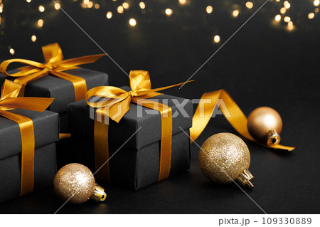 Black gift box with golden ribbon bow on black background 109330889