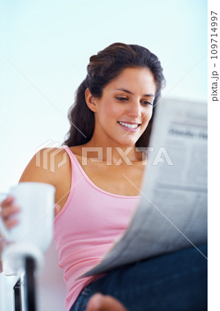 Happy woman, reading and newspaper with coffee and morning headlines for wellness in living room. Young person, smile and espresso to relax on weekend and current events with warm drink in apartment 109714997