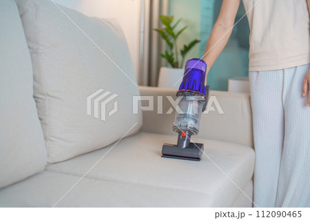 Woman cleaning Sofa with cordless Vacuum cleaner. Housewife using wireless Hoover for big cleaning home. Housework, Housecleaning, Housekeeping, Removes dust, Domestic hygiene and daily routine 112090465