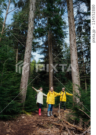 Group of hikers cheering joyful in forest. Cheerful excited friends with arms raised up outstretched in joy smiling, celebrating freedom and unity with nature. Tourism, hiking, and friendship concept. 114552880