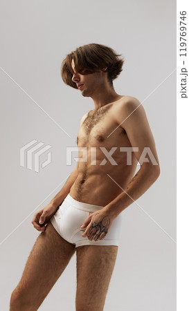 Side view portrait of young man with long hair, posing elegantly in underwear against grey studio background. 119769746