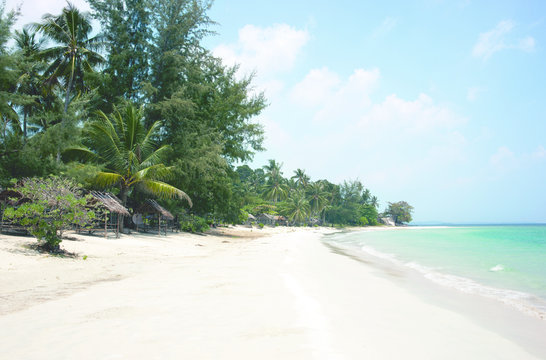 Tropical stretched out white sand beach and palm trees with blue colored ocean seashore water in the afternoon at Tanjung Pinang on Bintan island, Indonesia.