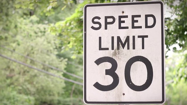 Camera pans to Speed Limit 30 sign near forested road