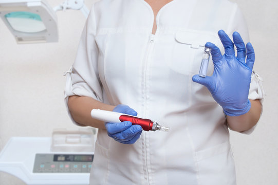 The cosmetologist in sterile gloves holds an electric appliance for mesotherapy of the facial skin and an ampoule with medicine. Close-up.