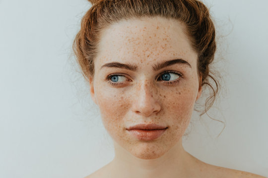 Woman portrait. Close-up. Beautiful blue eyed girl with freckles is looking away, on a white background