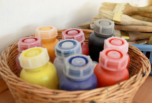 Cans with liquid watercolor in a basket on the background of wide brushes, art workshop on a sunny day