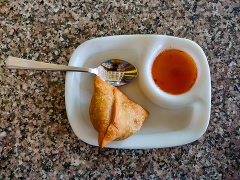 Samosa with chutney or sauce served in a white plate. Top view